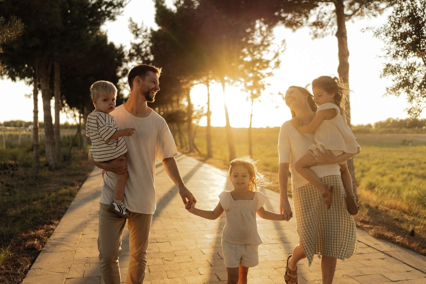 Família caminhando de mãos dadas por uma alameda ao pôr do sol.